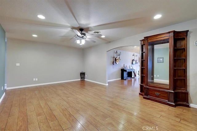 interior space featuring arched walkways, ceiling fan, visible vents, baseboards, and light wood finished floors