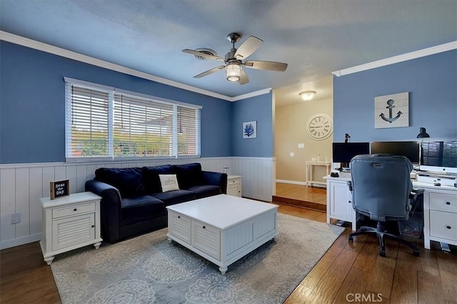 home office featuring ornamental molding, dark wood-style flooring, wainscoting, and a ceiling fan