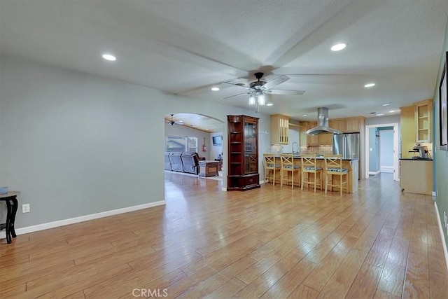 living room featuring light wood-style floors, baseboards, arched walkways, and a ceiling fan