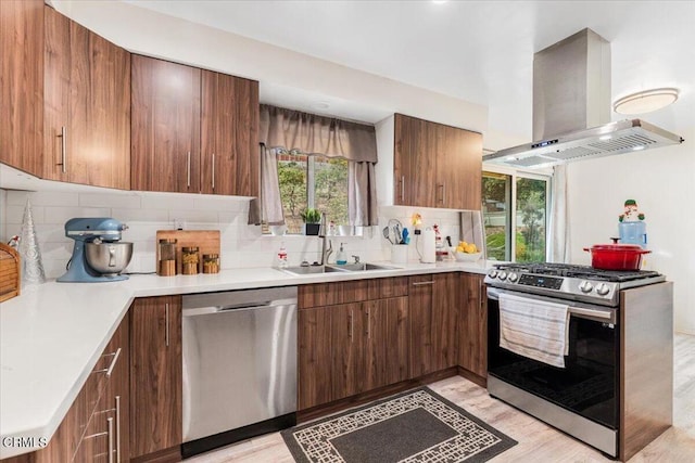 kitchen with sink, stainless steel appliances, island exhaust hood, light hardwood / wood-style floors, and decorative backsplash