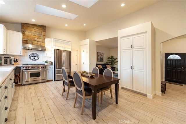 dining space featuring high vaulted ceiling, a skylight, and light hardwood / wood-style flooring