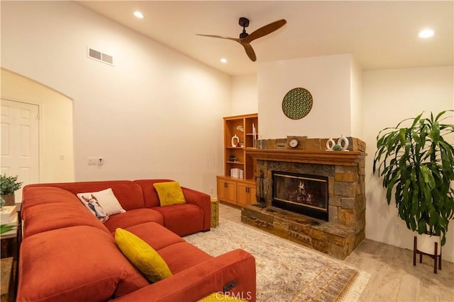 living room with a stone fireplace, ceiling fan, and light hardwood / wood-style flooring