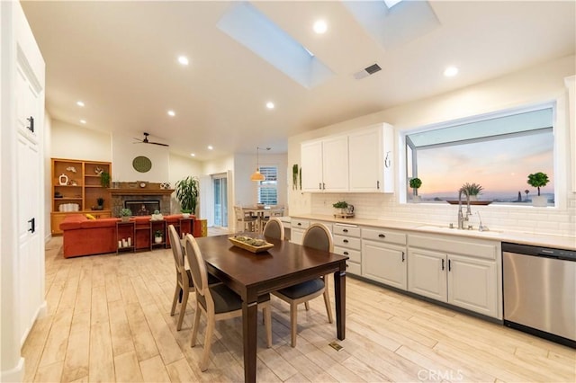 dining room featuring light hardwood / wood-style floors, lofted ceiling with skylight, ceiling fan, and sink