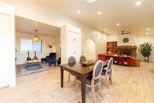 dining area with ceiling fan, a large fireplace, and light wood-type flooring