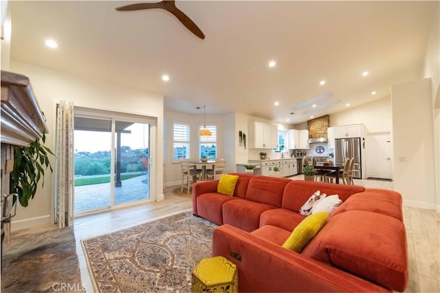 living room with ceiling fan, vaulted ceiling, and light wood-type flooring