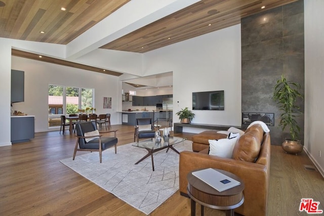 living room featuring hardwood / wood-style flooring, a tile fireplace, wooden ceiling, and high vaulted ceiling