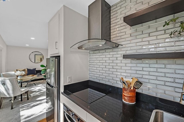 kitchen with white cabinetry, stainless steel fridge, wall chimney range hood, and wall oven