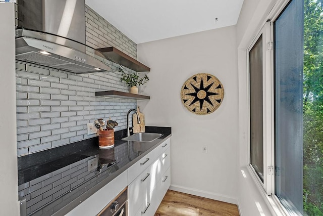 kitchen featuring sink, wall chimney exhaust hood, a healthy amount of sunlight, and light hardwood / wood-style floors