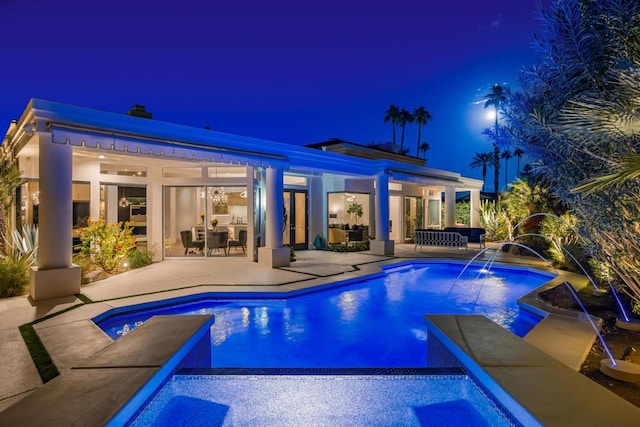 pool at night with pool water feature, outdoor lounge area, and a patio