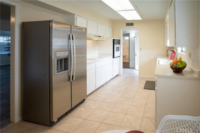 kitchen featuring white oven, sink, stainless steel refrigerator with ice dispenser, light tile patterned flooring, and white cabinetry