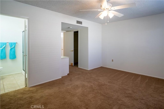 unfurnished bedroom featuring a textured ceiling, light colored carpet, ceiling fan, and ensuite bathroom