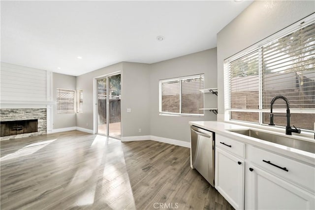 kitchen with white cabinetry, a stone fireplace, plenty of natural light, dishwasher, and sink