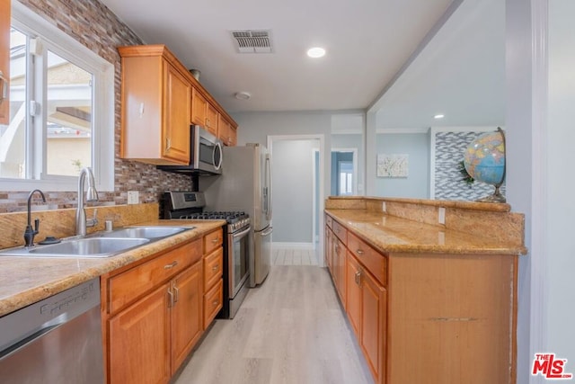 kitchen with sink, backsplash, stainless steel appliances, light stone countertops, and light hardwood / wood-style flooring