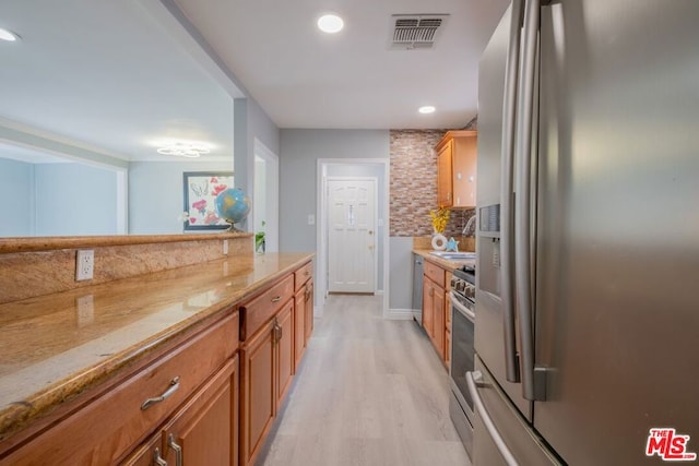 kitchen with sink, light hardwood / wood-style flooring, appliances with stainless steel finishes, backsplash, and light stone counters