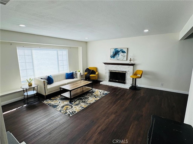 living room with a textured ceiling, dark hardwood / wood-style floors, and a stone fireplace