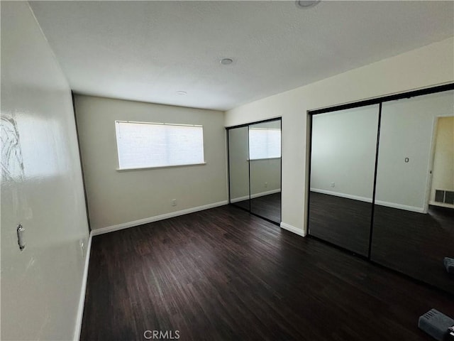 unfurnished bedroom with two closets and dark hardwood / wood-style floors