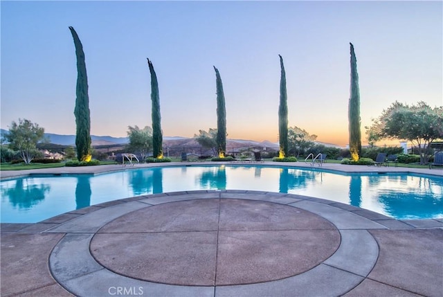 pool at dusk featuring a mountain view and a patio