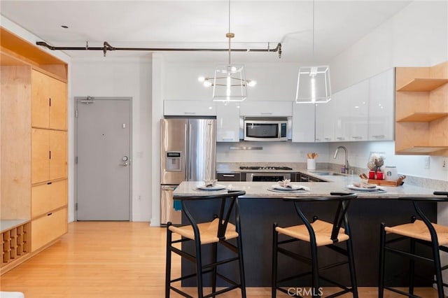 kitchen with stainless steel appliances, sink, white cabinetry, a kitchen breakfast bar, and pendant lighting