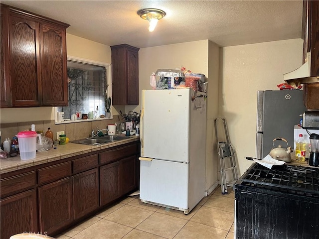 kitchen featuring light tile patterned floors, tile countertops, stainless steel fridge, white refrigerator, and sink