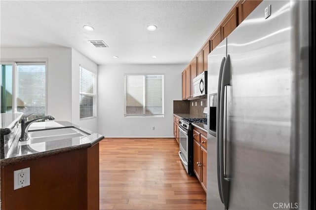 11465 Oakford Ln, Porter Ranch, CA 91326 - kitchen with stainless steel appliances, brown cabinetry, light wood-style floors, tasteful backsplash, and dark stone countertops