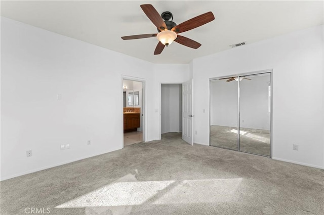 unfurnished bedroom with light carpet, a closet, ceiling fan, and ensuite bathroom