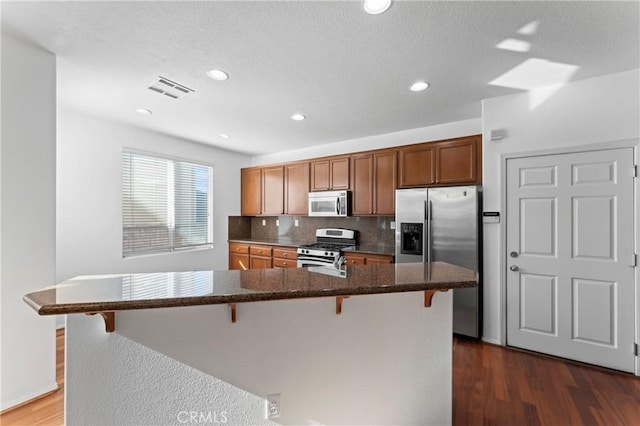 kitchen with dark hardwood / wood-style floors, a kitchen island, a breakfast bar area, and stainless steel appliances