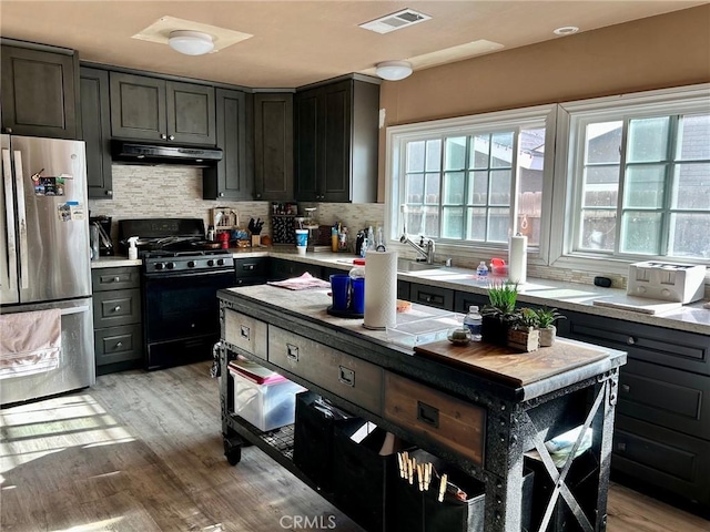 kitchen with decorative backsplash, a kitchen island, light wood-type flooring, gas stove, and stainless steel refrigerator