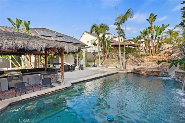 view of pool with a patio, pool water feature, and exterior kitchen