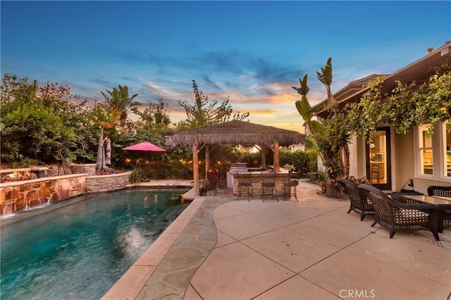 pool at dusk featuring a bar, a patio area, and a gazebo