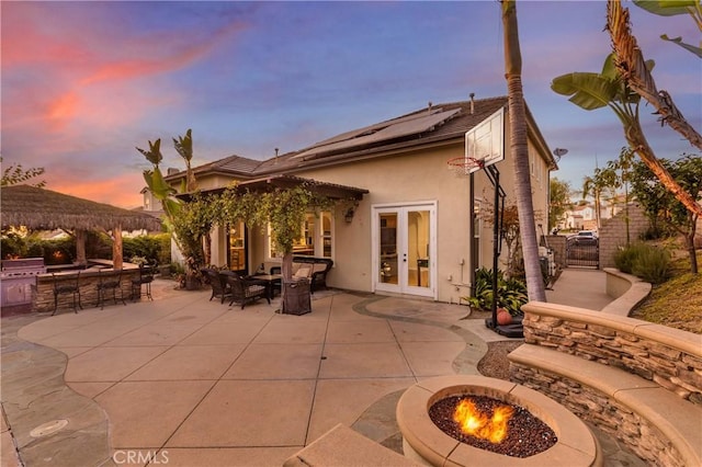 back house at dusk featuring french doors, exterior bar, a fire pit, and a patio