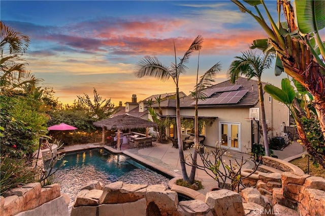 pool at dusk with a patio area and french doors