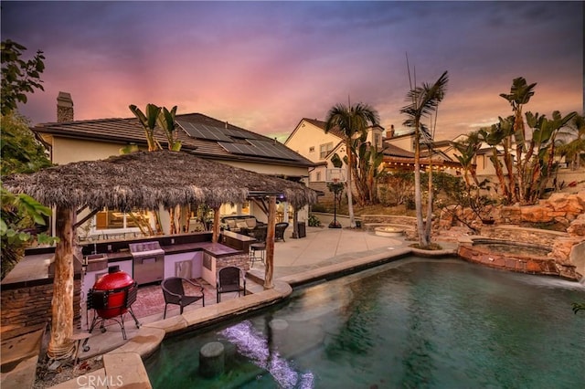 pool at dusk featuring an in ground hot tub, a patio, and a fire pit