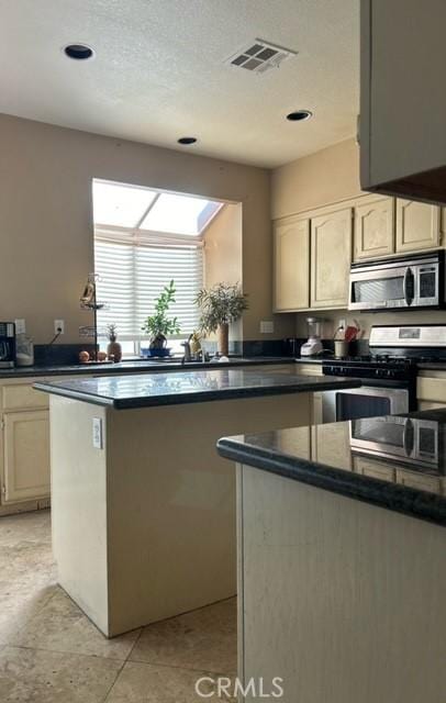 kitchen with a kitchen island, a textured ceiling, appliances with stainless steel finishes, and cream cabinets