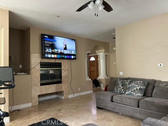 living room with decorative columns, a tiled fireplace, ceiling fan, and a textured ceiling