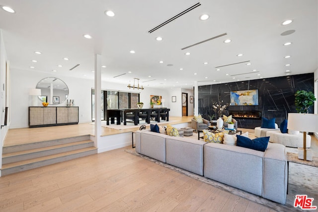 living room with a chandelier, light wood-type flooring, and a premium fireplace