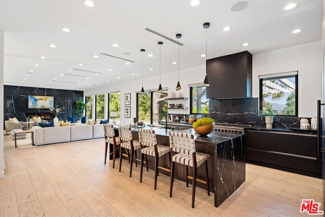 kitchen with light hardwood / wood-style flooring, wall chimney exhaust hood, tasteful backsplash, a large island, and a breakfast bar area