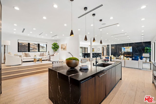 kitchen with dark brown cabinets, sink, a large island with sink, decorative light fixtures, and light hardwood / wood-style flooring