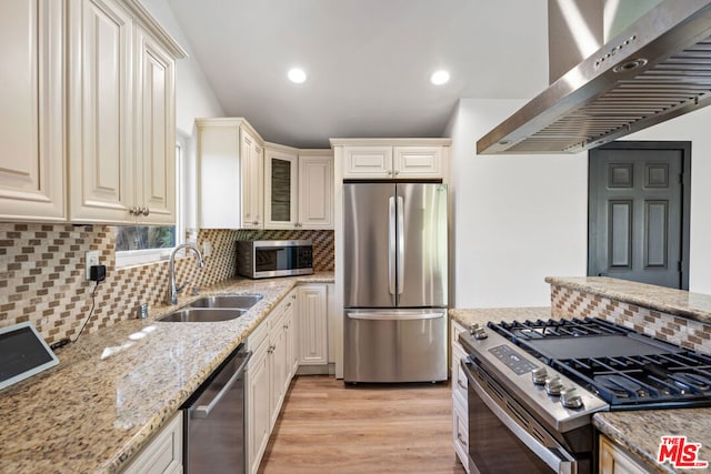 kitchen with sink, stainless steel appliances, light stone counters, range hood, and light wood-type flooring