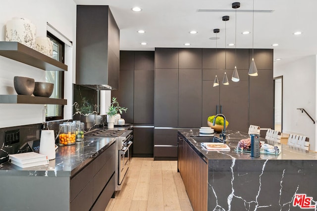 kitchen with wall chimney exhaust hood, sink, pendant lighting, light hardwood / wood-style flooring, and range with two ovens