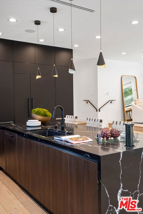 kitchen featuring light wood-type flooring, dark brown cabinetry, and decorative light fixtures