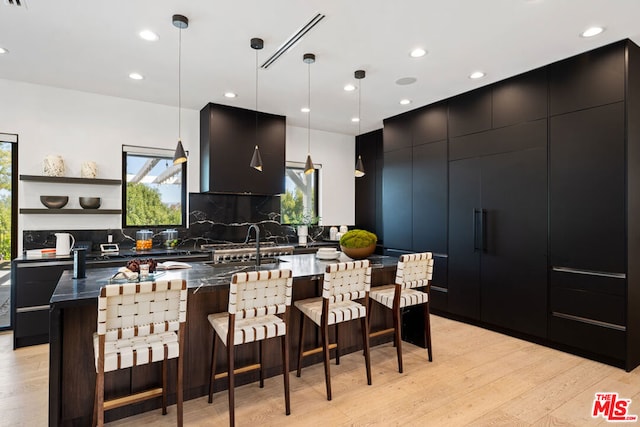 kitchen featuring a spacious island, wall chimney range hood, hanging light fixtures, tasteful backsplash, and light hardwood / wood-style floors