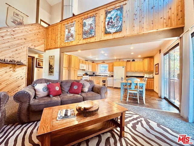 living room with a high ceiling, a wealth of natural light, wood walls, and light wood-type flooring