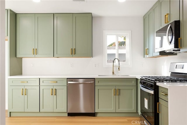 kitchen with stainless steel appliances, light hardwood / wood-style floors, green cabinets, and sink