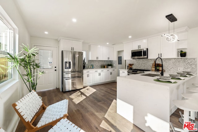 kitchen featuring sink, appliances with stainless steel finishes, kitchen peninsula, pendant lighting, and white cabinets