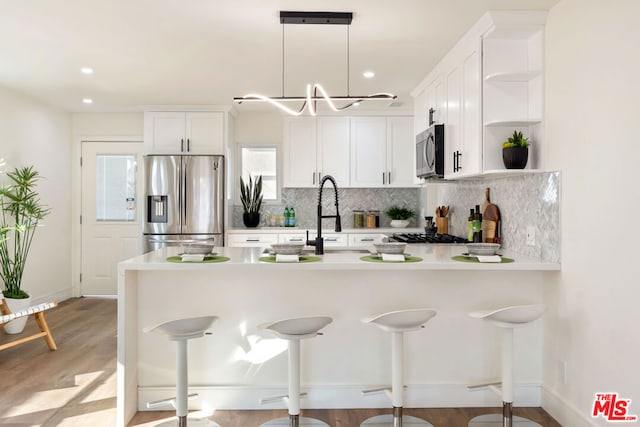 kitchen featuring white cabinetry, hanging light fixtures, a kitchen breakfast bar, kitchen peninsula, and stainless steel appliances