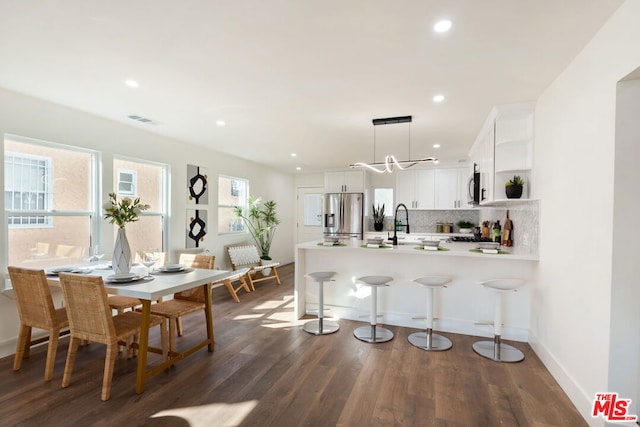 kitchen with appliances with stainless steel finishes, pendant lighting, white cabinets, dark hardwood / wood-style flooring, and kitchen peninsula