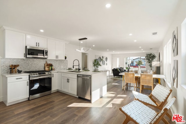 kitchen with appliances with stainless steel finishes, decorative light fixtures, white cabinetry, sink, and kitchen peninsula