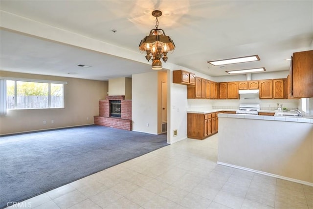 kitchen featuring hanging light fixtures, a brick fireplace, a notable chandelier, light colored carpet, and white stove