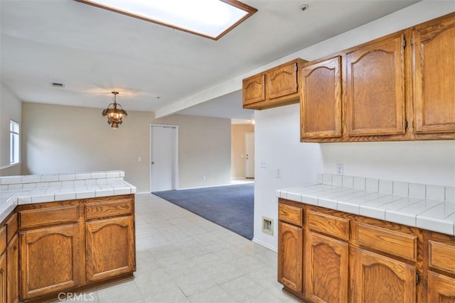 kitchen featuring tile countertops, kitchen peninsula, a chandelier, and decorative light fixtures