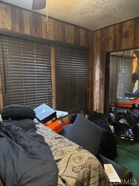 bedroom with ceiling fan, a textured ceiling, and wooden walls